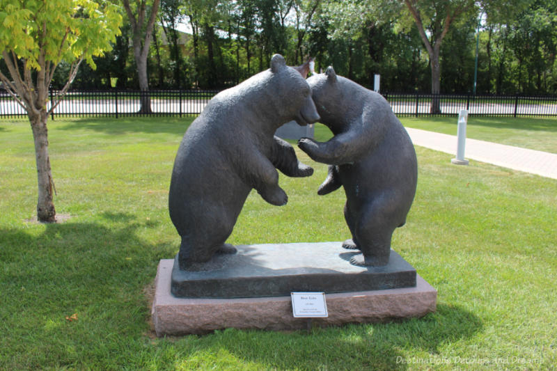 A sculpture in a park features two bear cubs on hind legs facing each other and almost hugging