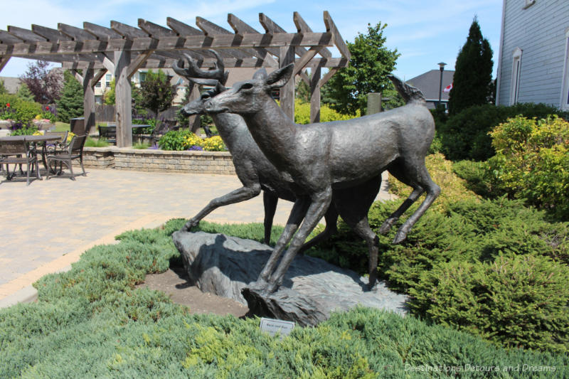 A sculpture of two deer (a buck and a doe) with a patio area containing a pergola, tables, and chair in the backgroun