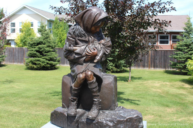 Bronze sculpture in a park showing a seated woman with a scarf on her head looking down at the young child she is holding