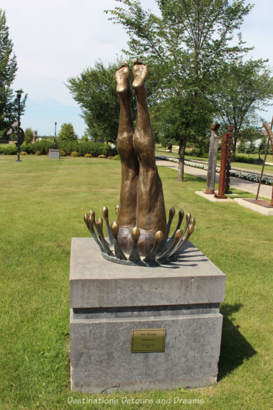 A bronze sculpture of a person's legs pointed upwards and mounted on a cement block in a way that looks as if the upper part of the body had plunged into the block