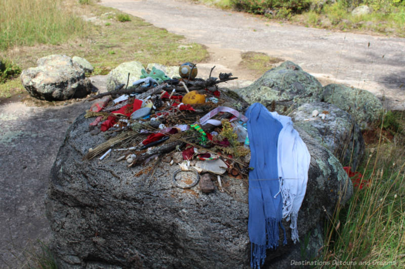 A rock at a petroforms site with a variety of ceremonial offerings (tobacco, ribbons, cloth, etc.) on it