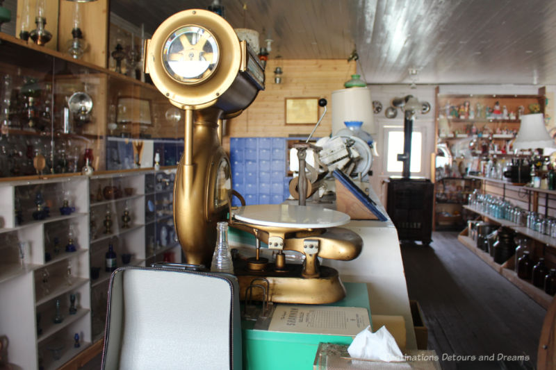 Interior of an old store at a museum with a scale on counter in forefront and rows of shelving containing artifacts