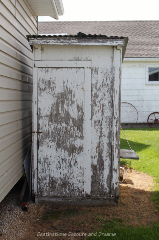 Old white outhouse with much of the paint peeled and worn off