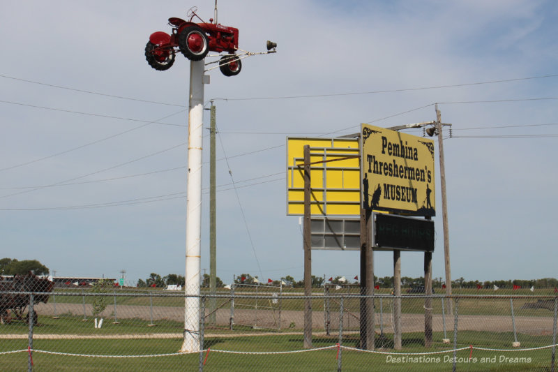 Pembina Threshermen's Museum sign beside a red tractor atop a pole