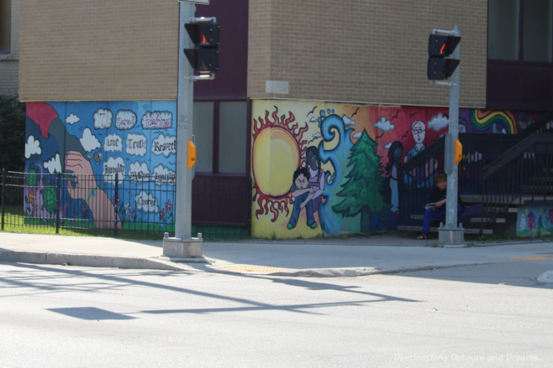 Mural covering the bottom part of two side of a building with a collage of items related to the theme of helping others