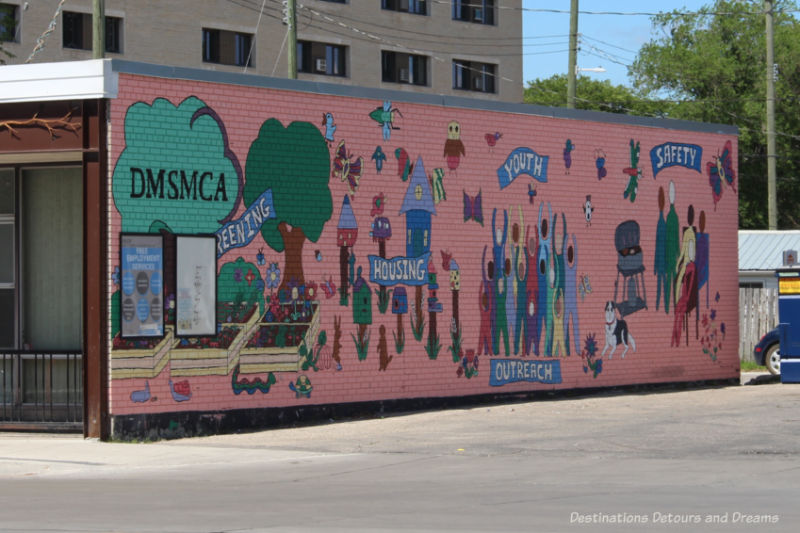 Mural on side of building with pink background and associated images associated with community needs of housing, outreach, and safety