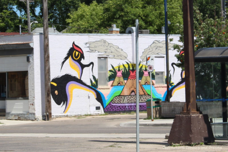 Indigenous style of art in a mural on the outside of building shows teepees and stylized animals