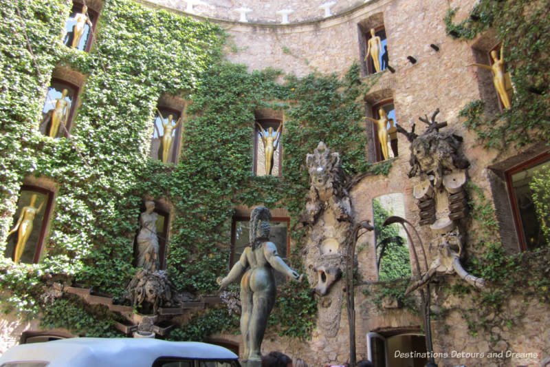 Ivy-covered brick wall in a circular courtyard with carved gargoyles and gold figurines in indented window ledges at the Dali-Theatre Museum