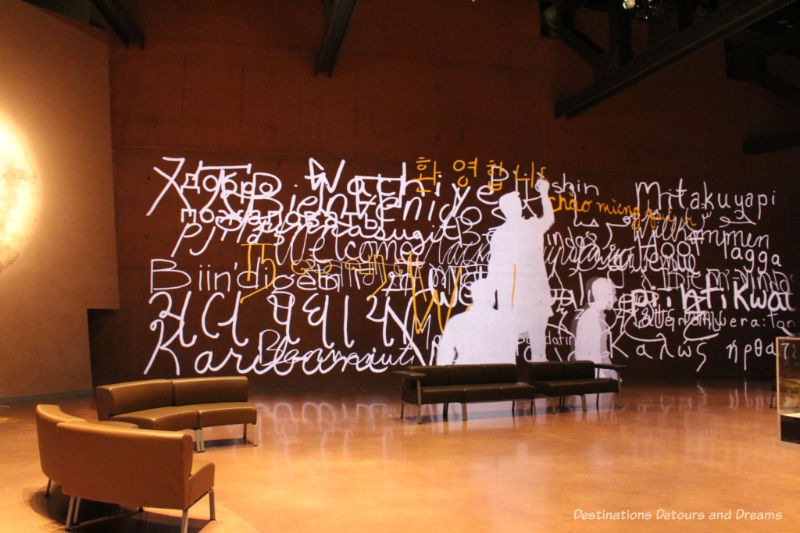 Projection of people writing welcome in many languages along a wall in a lobby