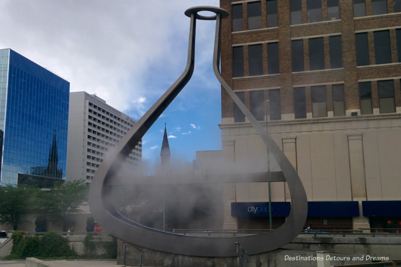 A public art piece that is the outline of a giant beaker with steam expelling from the inside