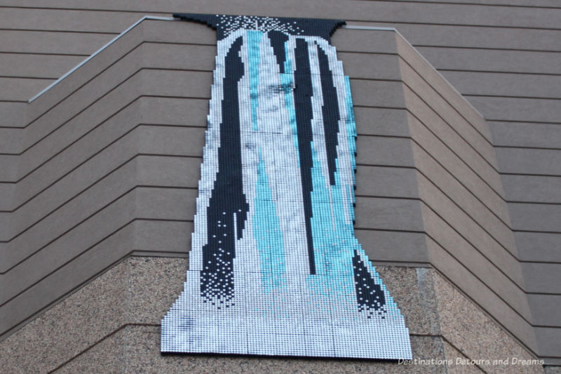 Cascading colours of white, aqua, and blue-black in a public art piece hanging on the outside of a Winnipeg building simulate a waterfall