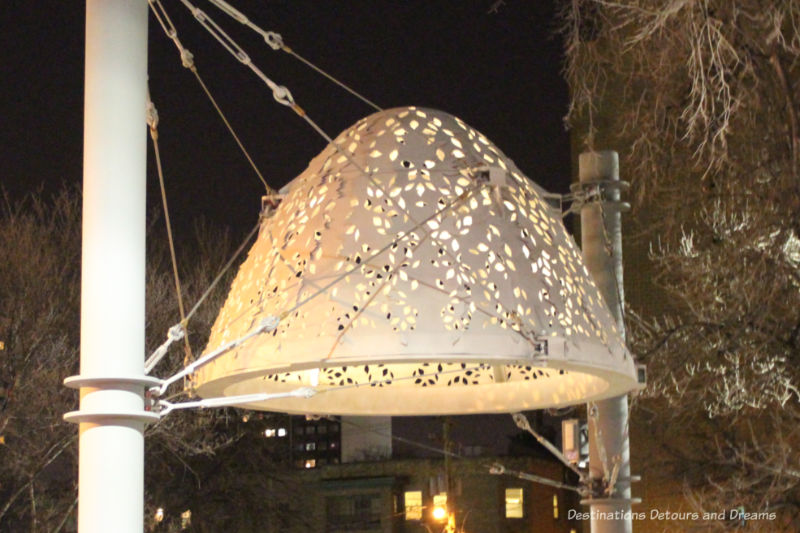 A steel dome public art piece with leave cutouts lit up at night in Winnipeg, Manitoba