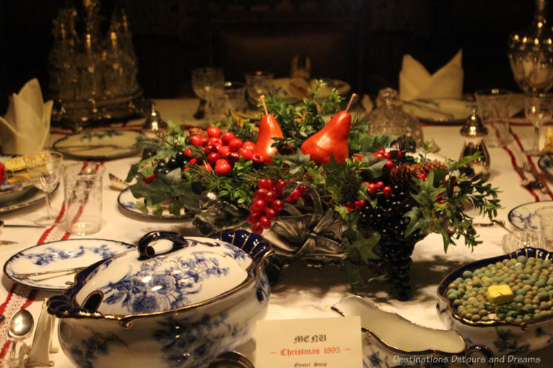 Victorian-era Christmas table with centerpiece of greenery, red berries, and red pears.