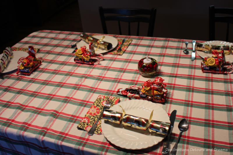 Table set for Christmas dinner with red, green, and white table cloth, white plates, Christmas crackers, mini-sleights of candies