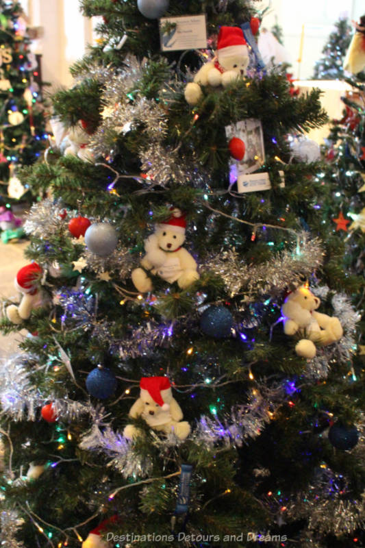 A Christmas tree decorated with a silver garland and little white teddy bear with red hat ornaments