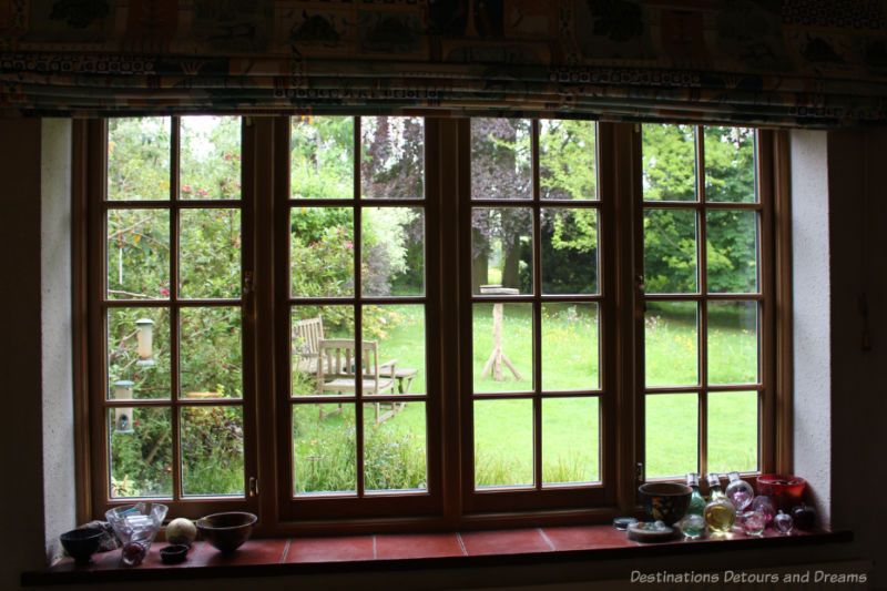 Lattice-paned window looking onto green lawn and trees of an English garden