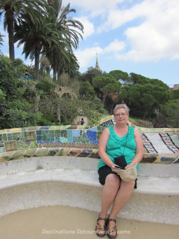 Sitting along a curved bench decorated with mosaic tiles at Park Guell