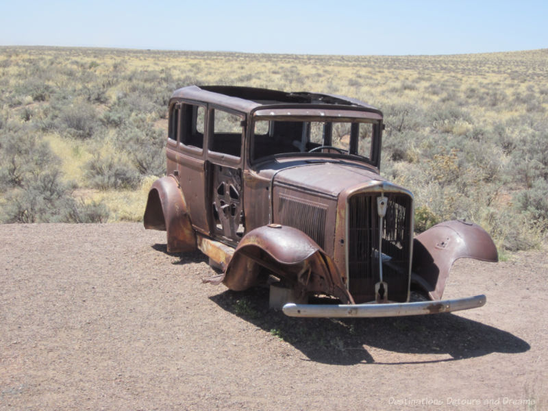 Old rusted car missing tires and doors sitting a gravel pull-out in the badlands of Petrified Forest National Park