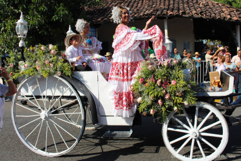 Woman in a white and red pollera dress riding in an open white carriage