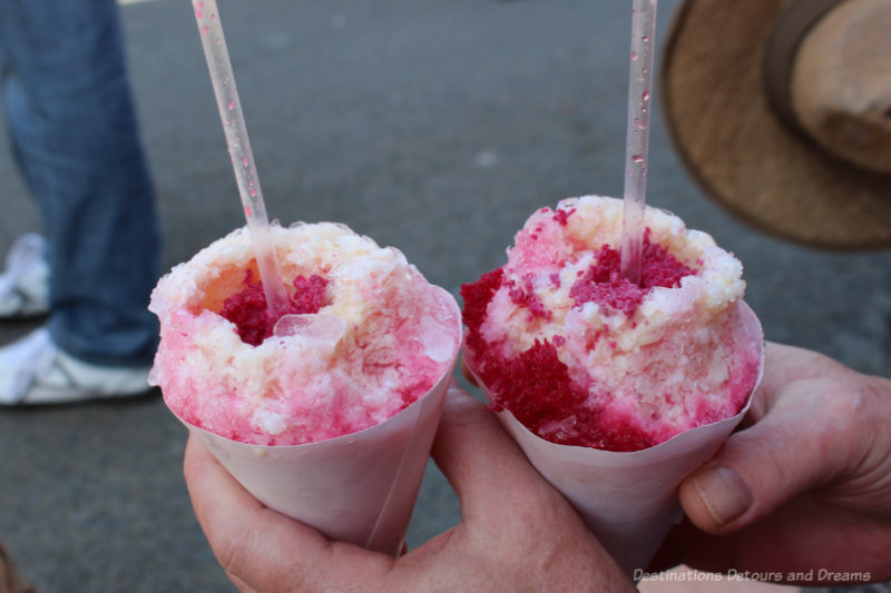 Two rasapados, paper cones filled with shaved ice and flavoured with sweet syrup and covered with flakes of coconut