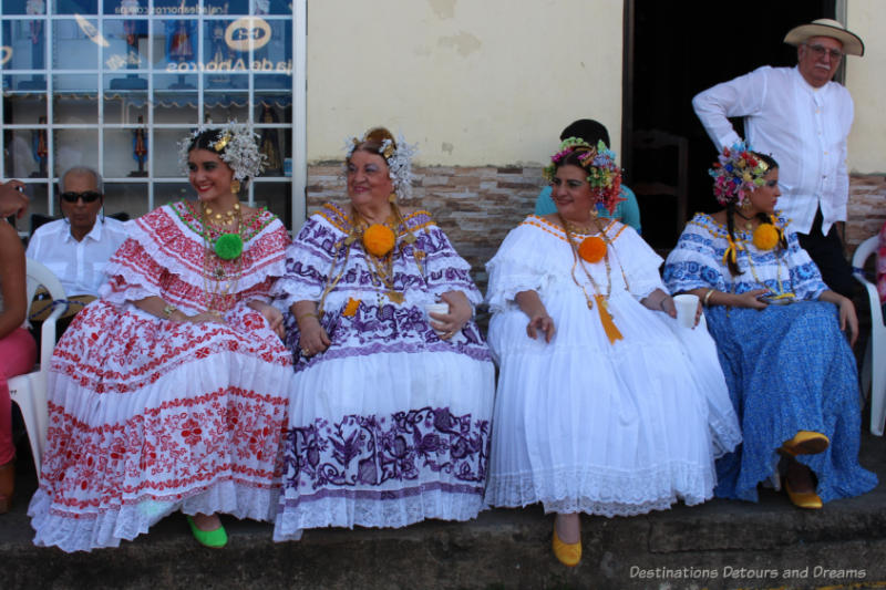 Four women in traditional Panamanian polleras seated and waiting for the Thousand Polleras Parade