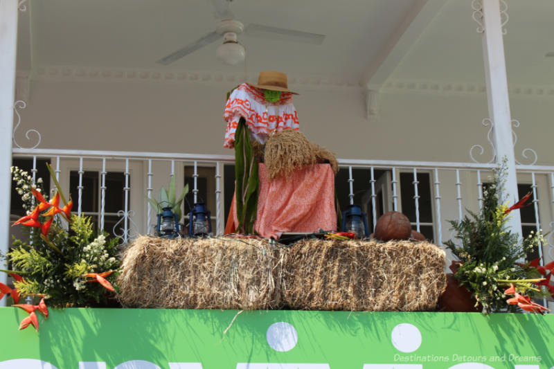 Decorations on the second level balcony of building in Las Tablas, Panama featuring a seated woman in traditional dress on a bale of hay flanked by floral bouquets