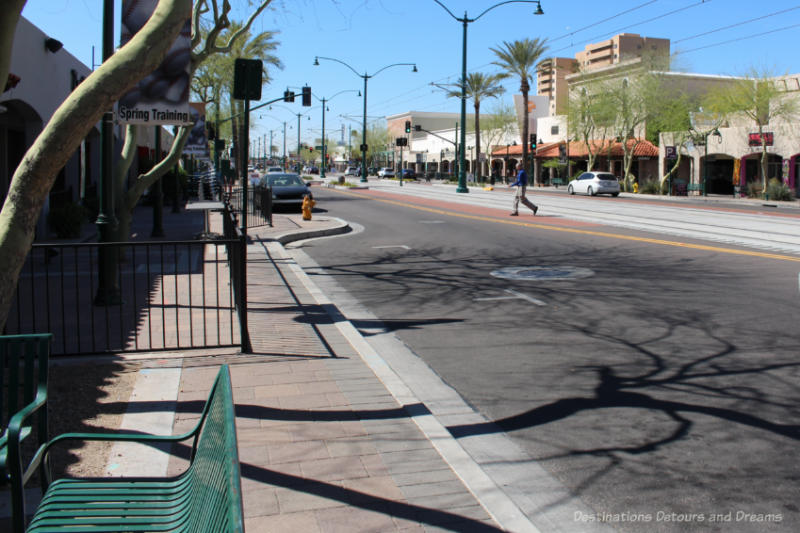 Wide main street of downtown Mesa, Arizona lined with low-rise buildings and with light rail system running through middle.