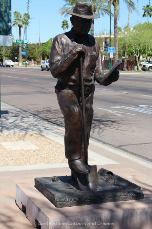 Sculpture of a man with his foot on a spade held with one hand and a paper in his other hand