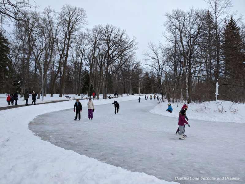 Skaters on a frozen park and people walking the path around the pond in a treed park