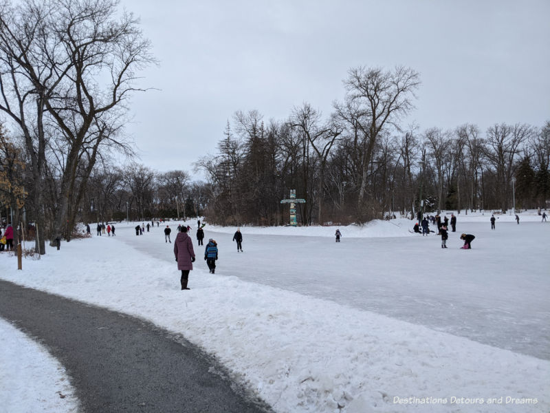 Path around a frozen skating pond, trees in the background along with a painted totem pole