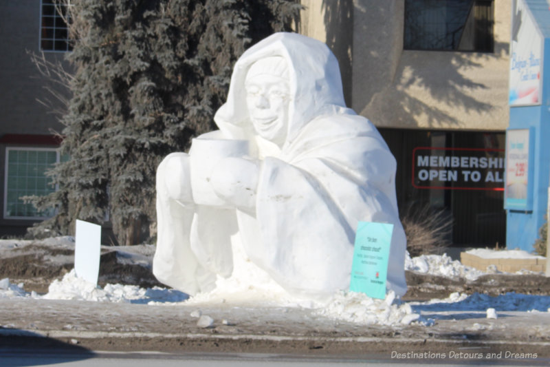 Snow sculpture of person sitting with a mug of hot chocolate