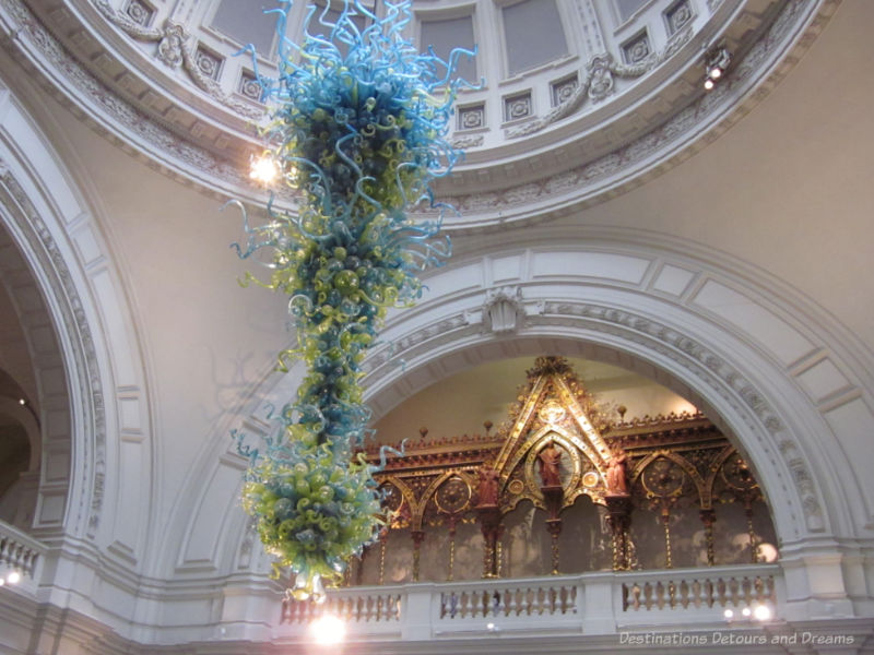 Chandelier of green and blue glass balls and spikes by Dale Chihuly hanging in entrance of Victoria and Albert Museum