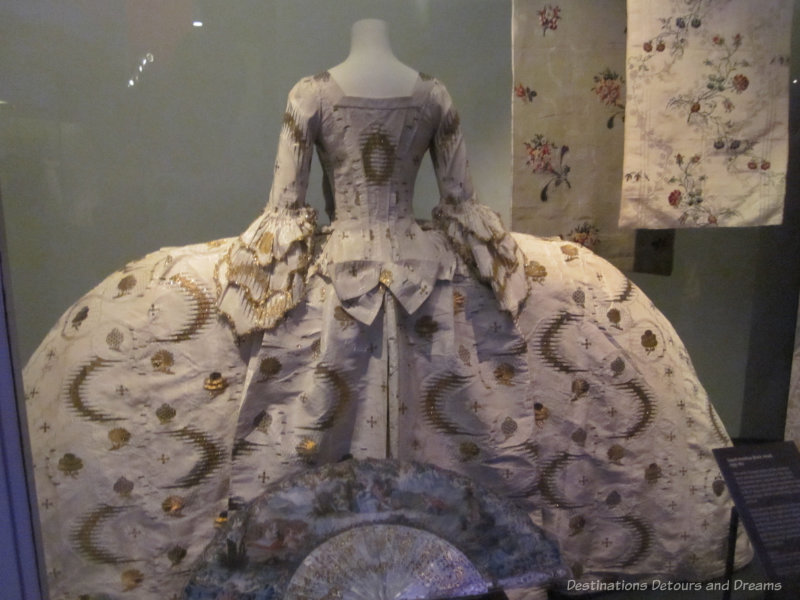 Wide-skirted brocade dress in white with gold embroidery worn by woman of court in England in 18th century