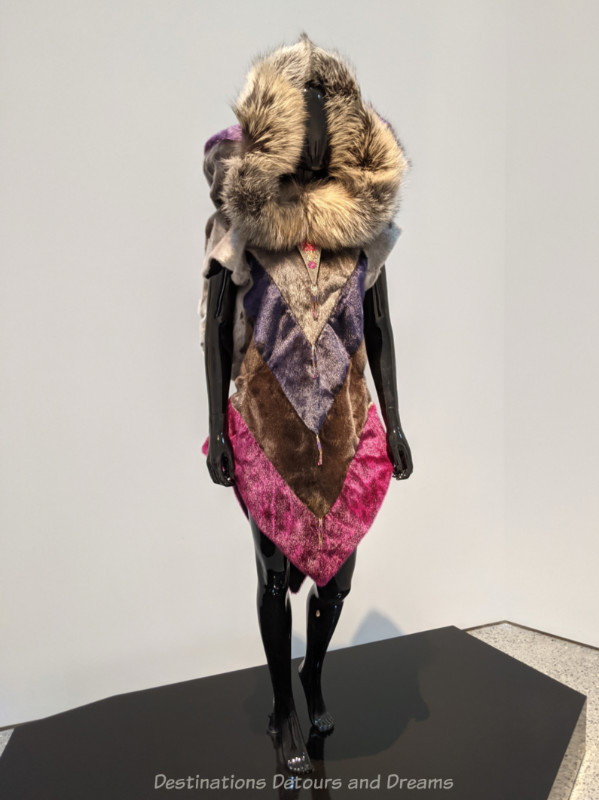 Inuit art piece: dyed sealskin coat with v-shaped stripes of pink, browns, and purple with a fox fur hood