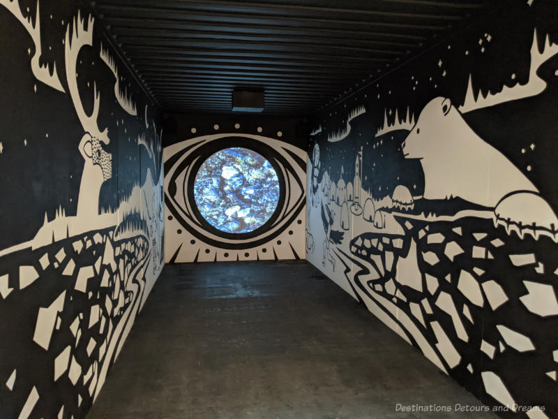 Inside of a shipping container painted with a black background and white images of a northern scene by Inuit artist Glenn Gear