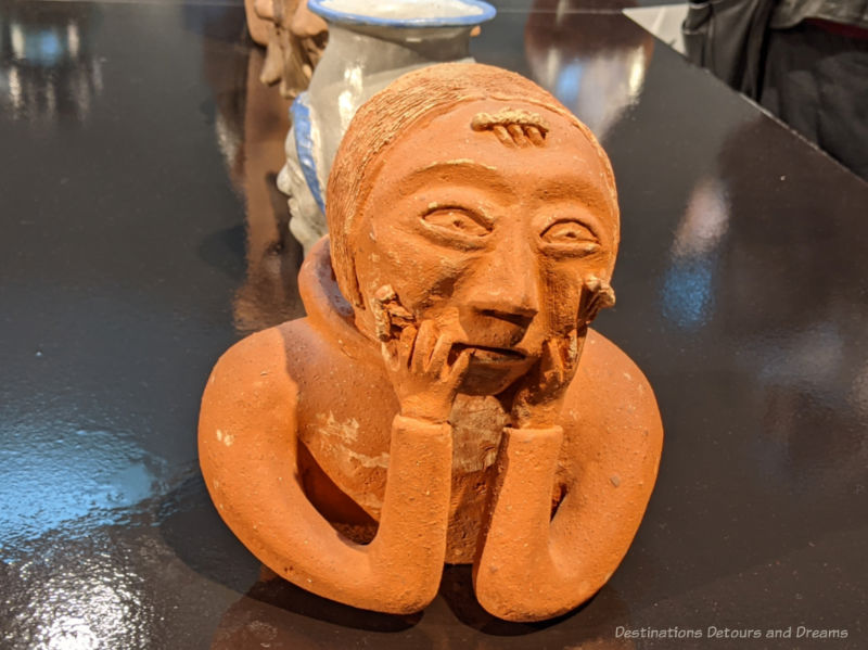 Clay sculpture of a woman's face resting  on her hands entitled Woman with Lice on Face by Donat Anawak