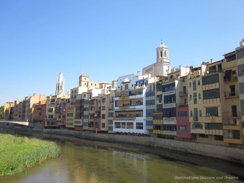 Four and five story row buildings painted in colourful colours lining the River Oynar in Girona