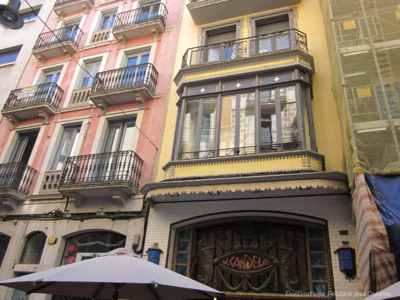 Pinkish and yellow exteriors of multi-story buildings with iron railed balconies in the Modernisme style in Girona