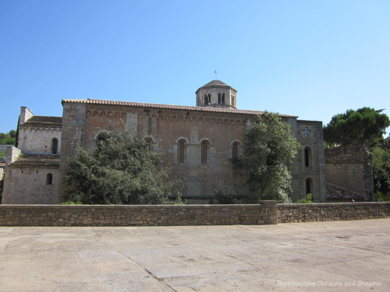 Stone Benedictine monastery building with an octagonal bell tower atop terra cotta roof in Girona