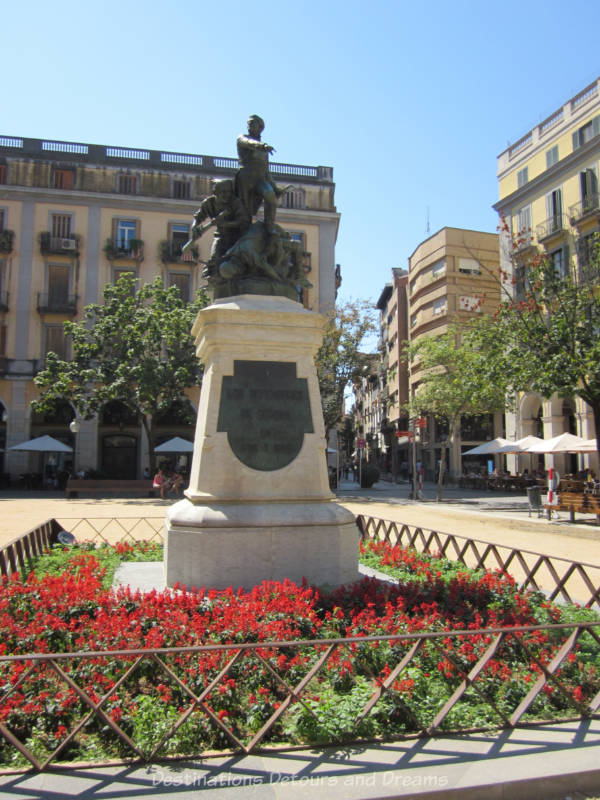 Statue of soldiers on a stone base surrounded by red flowers