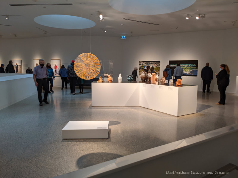 Qaumajuq Gizhig/Kisik A mezzanine level art gallery with a central table of Inuit carvings and art on the walls