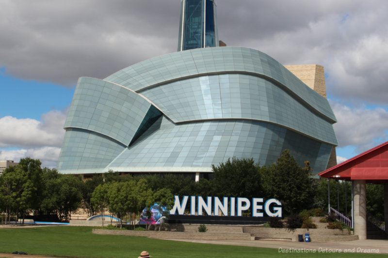 Winnipeg sign in front of the glass panels of the wings of Canadian Museum for Human Rights building in Winnipeg, Manitoba, Canada