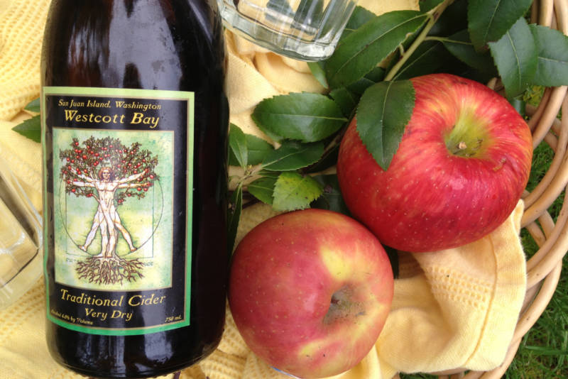 Bottle of cider beside two red apples. Photo courtesy of San Juan Islands Visitors Bureau.