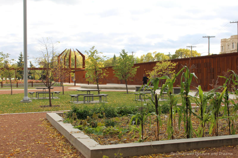 Park with raised beds, picnic table, and a weathered steel history fence running the length of the park in Upper Fort Garry, Winnipeg