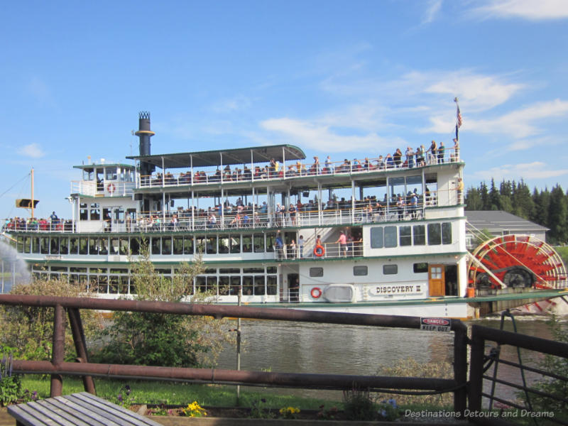 People inside and on the decks of a four-level sternwheeler cruising the river