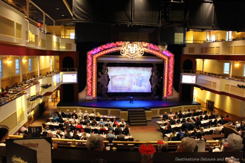 Showboat Branson Belle Stage Long dinner tables in front of a raised stage on the main floor of the Showboat Branson Belle area with balcony areas along the side