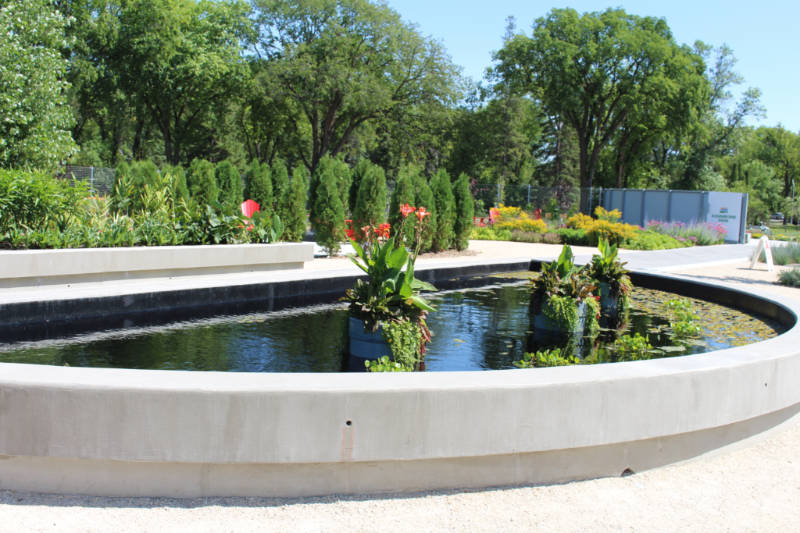 Cement half-circle shaped lily pond with path around it and gardens in the background