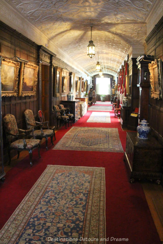 Long hallway with red carpeting covered with Persian rugs and art work hung along its wood panel walls