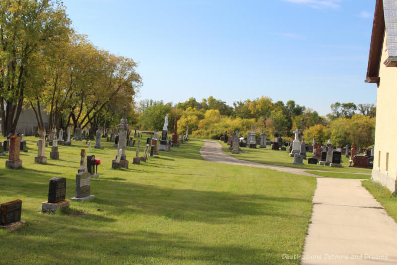 Cemetery on church grounds with trees turning fall colours in the backgroun