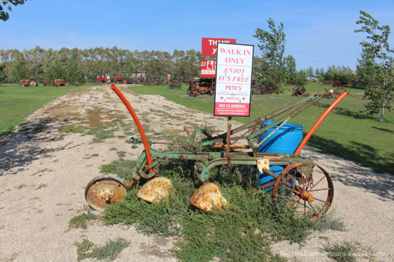 Rusted piece of machinery with sign saying Pete's leads to a field containing a collection of old machinery